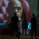 A scene from the original Matrix starring Laurence Fishburne plays on a screen in front of characters in The Matrix Resurrections.